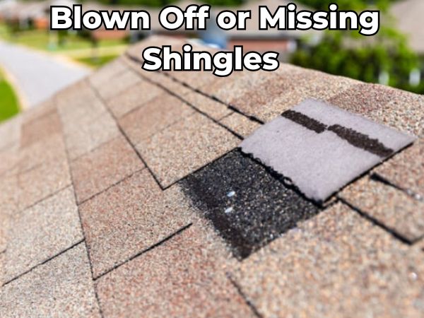 Close-up of a residential roof with missing and blown-off asphalt shingles, exposing the underlayment — a common issue caused by wind damage that requires prompt roof repair.