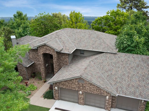 House with Malarkey Windsor Natural Wood shingle roof in warm brown, featuring brick siding and forested backdrop