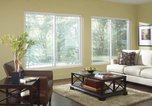 Sliding windows in a bright living room with light green walls, featuring a beige sofa, brown armchair, coffee table, and a scenic outdoor view.