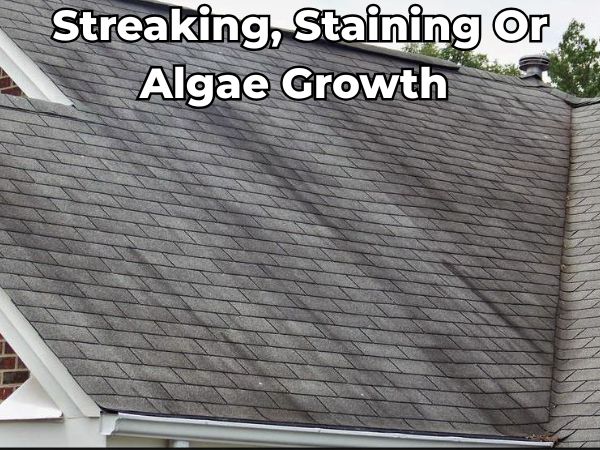 Residential asphalt roof with visible black streaks, staining, and algae growth — signs of moisture retention and aging that can impact roof performance and curb appeal.