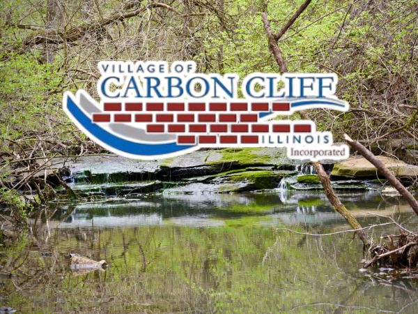 Scenic river with a 'Village of Carbon Cliff, Illinois Incorporated' sign featuring a brick graphic, for a Carbon Cliff, IL roofing, windows, and siding company.