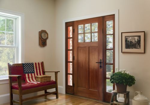 Wooden entry door with six glass panels in a cozy living room, featuring an American flag blanket on a chair, a clock, and potted plants.