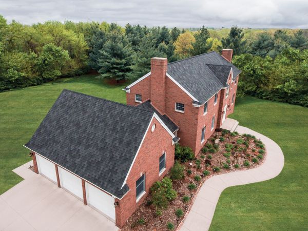 House with Malarkey Windsor Midnight Black shingle roof in solid black, featuring brick siding and forested surroundings