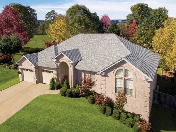 House with Malarkey Silverwood asphalt shingle roof in light gray with wood-like tones, surrounded by autumn trees