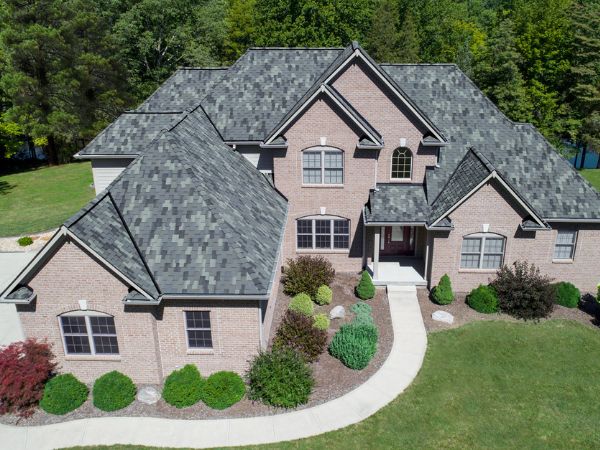 House with Malarkey Windsor Storm Grey shingle roof in medium gray, featuring brick siding and lush greenery