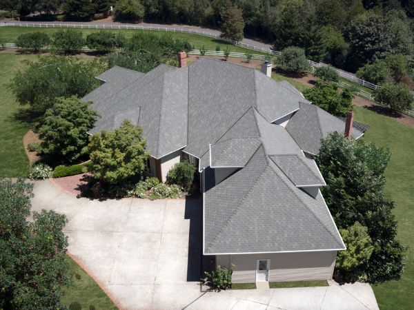 House with Malarkey Windsor Weathered Wood shingle roof in gray-brown, surrounded by greenery and a white fence