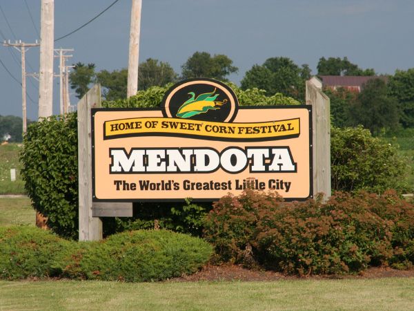 Mendota sign announcing the Sweet Corn Festival and "The World's Greatest Little City" with corn graphic and greenery